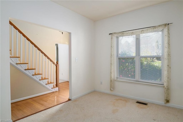 spare room featuring visible vents, carpet floors, baseboards, and stairs