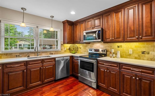kitchen with appliances with stainless steel finishes, a sink, dark wood-style flooring, light countertops, and decorative light fixtures