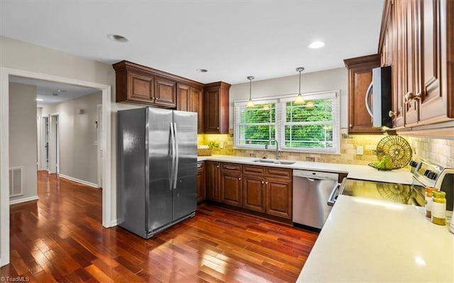 kitchen featuring appliances with stainless steel finishes, a sink, light countertops, dark wood-style floors, and decorative backsplash