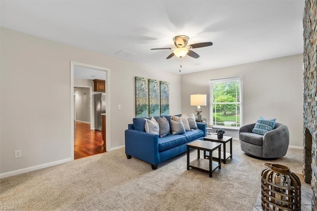 living area featuring light carpet, a ceiling fan, and baseboards