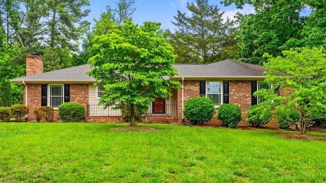 view of front of house with a chimney, a front yard, brick siding, and a shingled roof