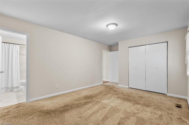 unfurnished bedroom with carpet flooring, baseboards, a closet, and ensuite bathroom