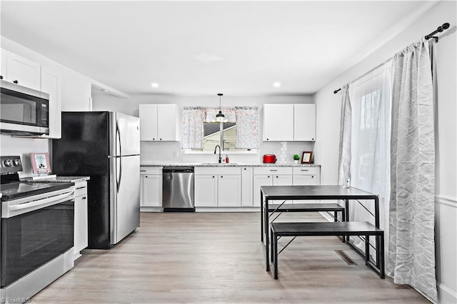 kitchen featuring sink, light hardwood / wood-style flooring, white cabinetry, hanging light fixtures, and stainless steel appliances