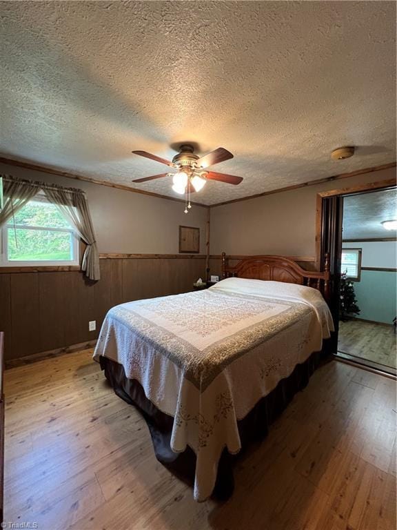 bedroom featuring light wood-type flooring, wainscoting, ceiling fan, and a textured ceiling