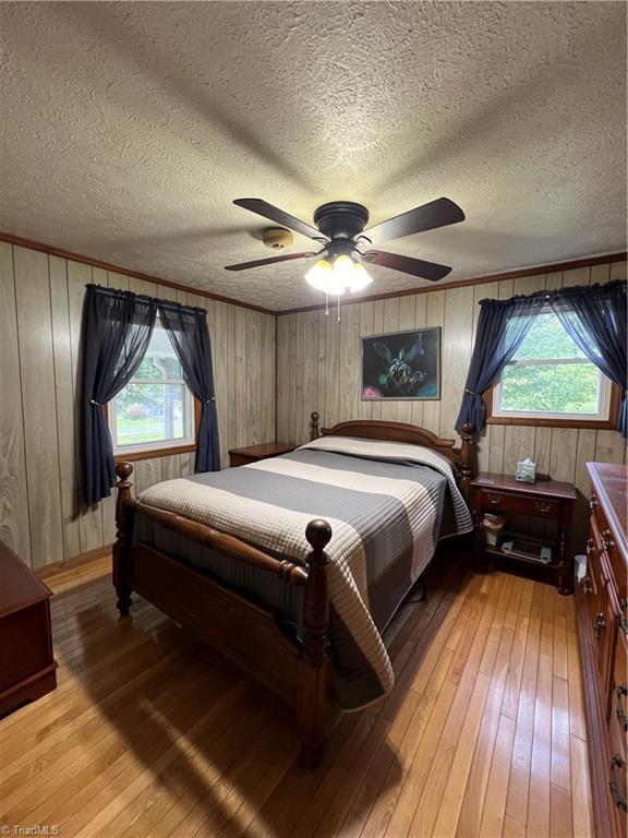 bedroom with light wood-type flooring, ceiling fan, ornamental molding, and a textured ceiling