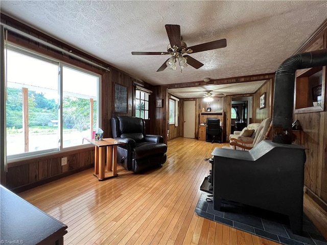 living area featuring a wood stove, wooden walls, light wood finished floors, and a textured ceiling