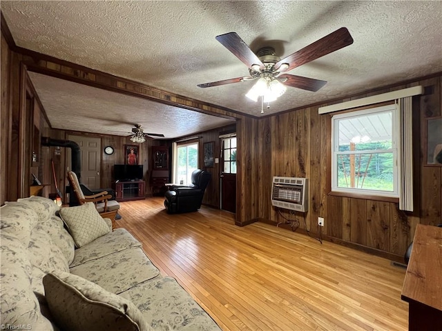 unfurnished living room with a textured ceiling, wooden walls, a ceiling fan, light wood-type flooring, and heating unit