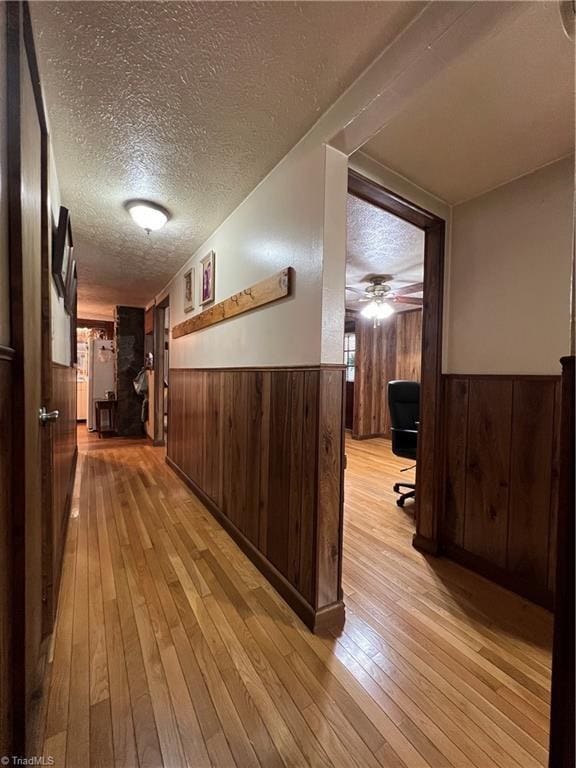 corridor featuring a wainscoted wall, a textured ceiling, light wood-style flooring, and wooden walls