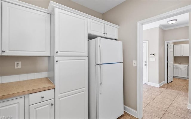 kitchen with white cabinets, white refrigerator, ornamental molding, and light tile patterned flooring