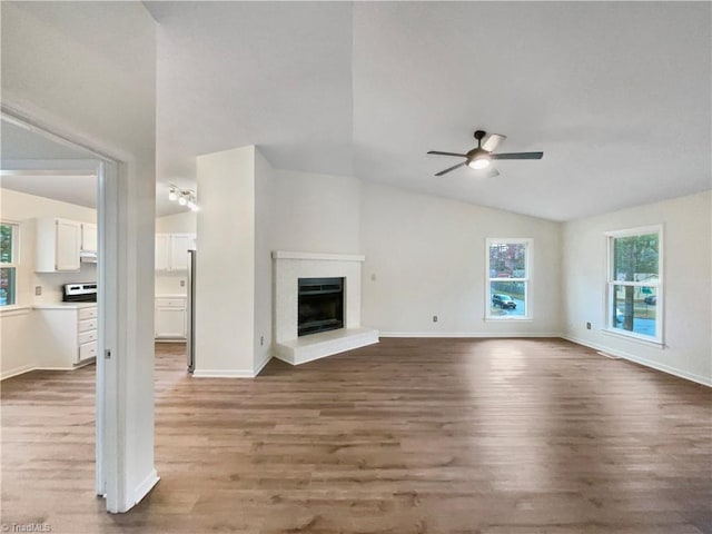 unfurnished living room featuring a fireplace with raised hearth, baseboards, lofted ceiling, wood finished floors, and a ceiling fan