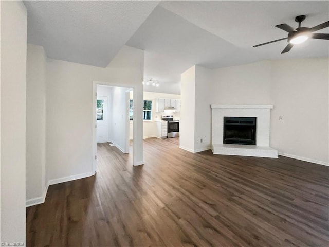 unfurnished living room featuring a brick fireplace, baseboards, dark wood-style flooring, and ceiling fan