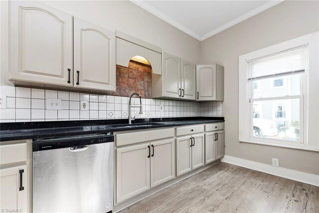 kitchen with ornamental molding, decorative backsplash, stainless steel dishwasher, a sink, and dark countertops