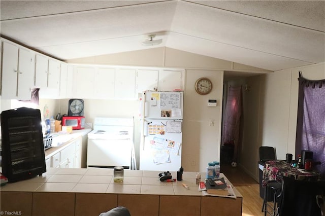 kitchen with light hardwood / wood-style flooring, vaulted ceiling, white refrigerator, washer / dryer, and white cabinetry