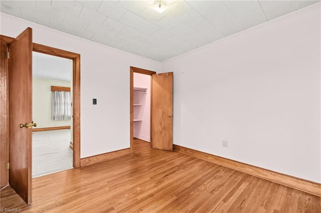 unfurnished bedroom with light wood-type flooring, a spacious closet, a closet, and ornamental molding