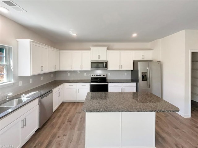 kitchen featuring stainless steel appliances, light wood-style floors, backsplash, a sink, and a center island