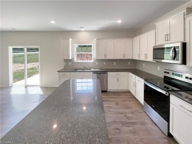 kitchen with dark stone counters, a sink, tasteful backsplash, white cabinetry, and appliances with stainless steel finishes