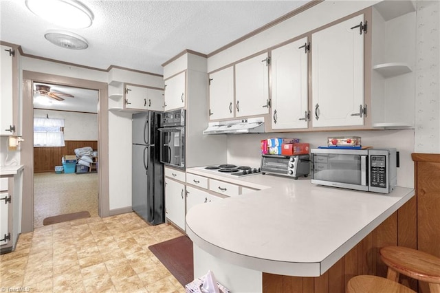 kitchen with white cabinetry, black appliances, kitchen peninsula, and wood walls