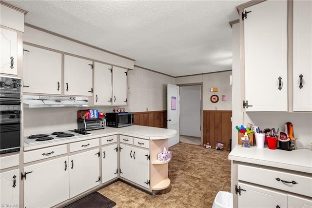 kitchen with black oven, white cabinetry, white electric cooktop, a textured ceiling, and wood walls