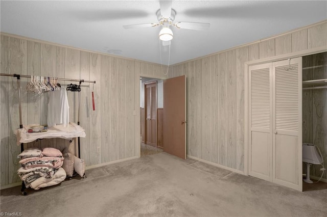 unfurnished bedroom with wooden walls, light carpet, ceiling fan, and a closet