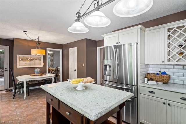 6404 Muirfield Dr, Greensboro, NC 27410 - kitchen featuring stainless steel fridge, decorative backsplash, white cabinetry, decorative light fixtures, and light stone counters