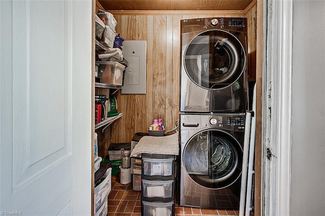 clothes washing area with stacked washer / drying machine, electric panel, and wood walls