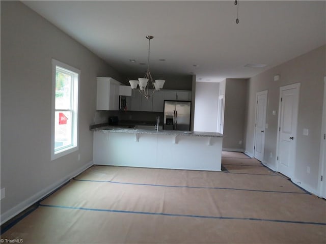 kitchen with kitchen peninsula, light stone countertops, decorative light fixtures, a notable chandelier, and stainless steel fridge