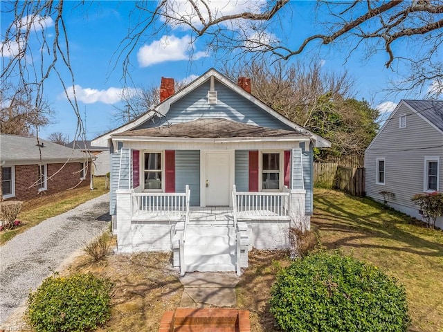 bungalow-style home with a porch, fence, a front yard, a shingled roof, and a chimney