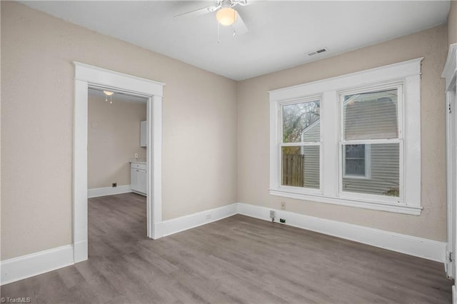 unfurnished room with ceiling fan, wood finished floors, visible vents, and baseboards