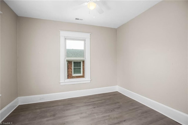 empty room with dark wood finished floors, visible vents, a ceiling fan, and baseboards