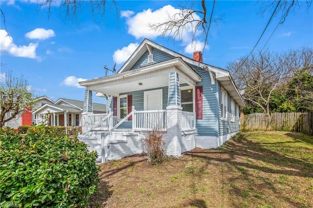 view of front of home with a front lawn, fence, covered porch, and a chimney