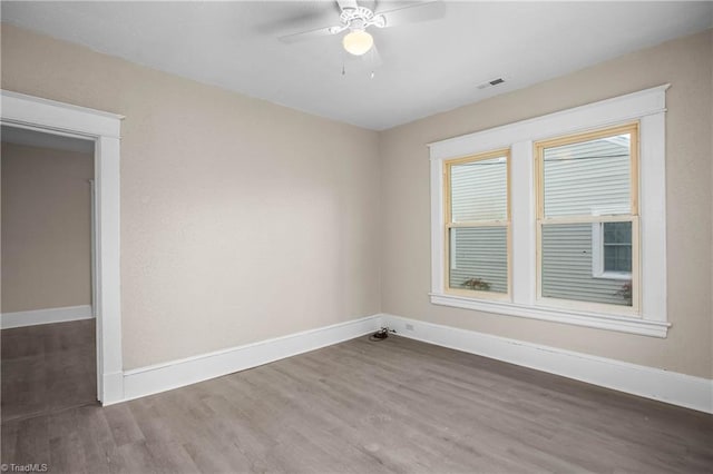 spare room featuring ceiling fan, visible vents, baseboards, and wood finished floors