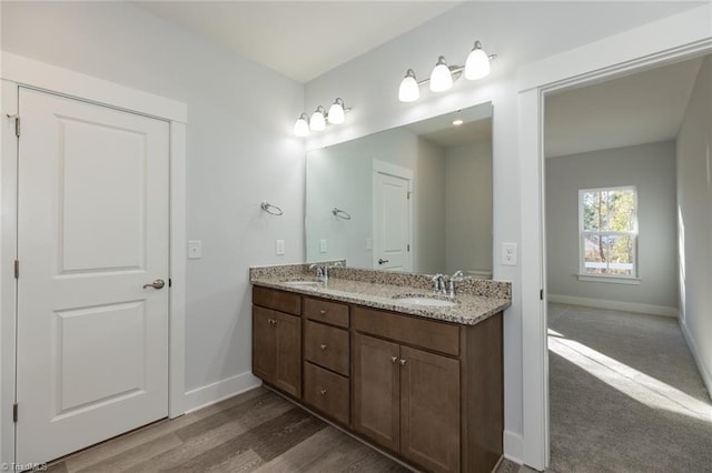 bathroom featuring wood finished floors, a sink, baseboards, and double vanity