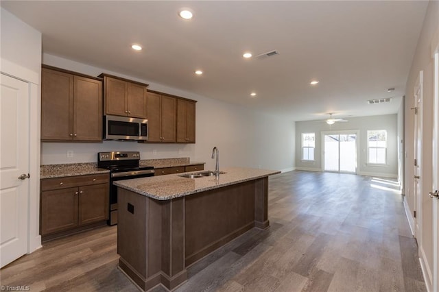 kitchen with dark wood-style floors, appliances with stainless steel finishes, light stone countertops, a sink, and recessed lighting