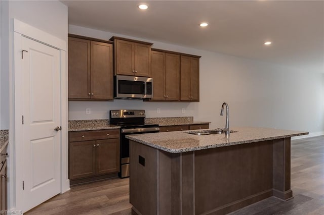 kitchen with light stone counters, recessed lighting, a sink, appliances with stainless steel finishes, and dark wood-style floors