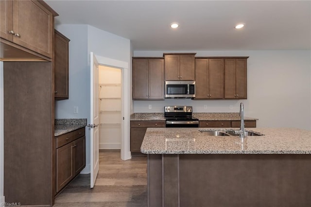 kitchen featuring recessed lighting, dark wood-style flooring, a sink, appliances with stainless steel finishes, and light stone countertops