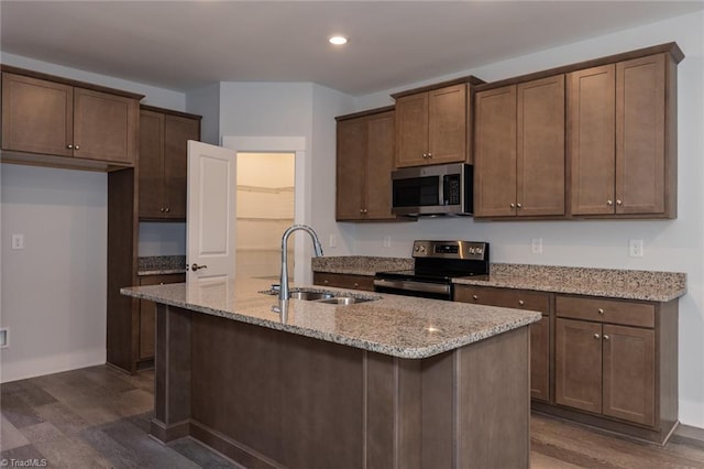 kitchen featuring appliances with stainless steel finishes, dark wood-type flooring, a sink, and light stone countertops