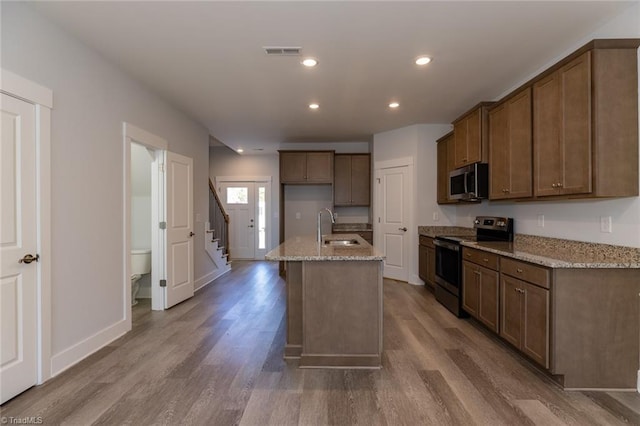 kitchen featuring wood finished floors, visible vents, appliances with stainless steel finishes, a sink, and light stone countertops