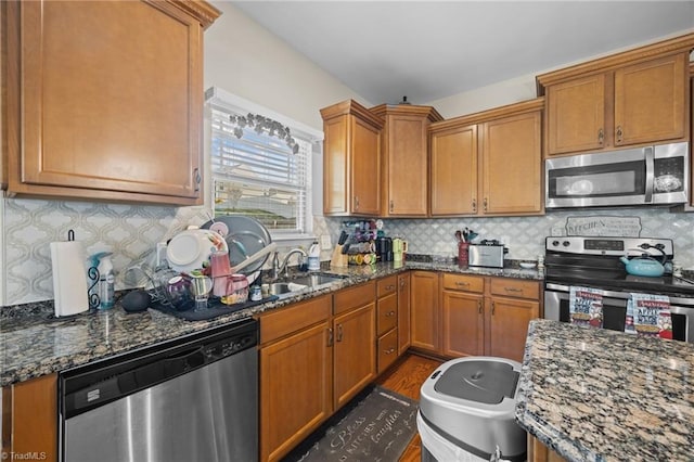 kitchen with stainless steel appliances, dark stone counters, and brown cabinets