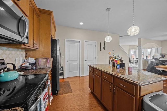 kitchen featuring stainless steel appliances, ornate columns, tasteful backsplash, dark stone counters, and a kitchen island
