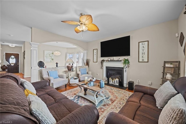 living room featuring a ceiling fan, wood finished floors, a glass covered fireplace, decorative columns, and baseboards