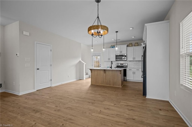 kitchen featuring stainless steel appliances, a center island with sink, white cabinets, light hardwood / wood-style floors, and hanging light fixtures