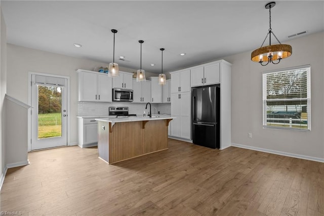 kitchen with stainless steel appliances, pendant lighting, a center island with sink, light hardwood / wood-style floors, and white cabinetry