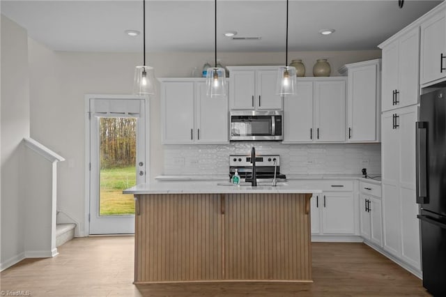 kitchen featuring stainless steel appliances, hanging light fixtures, and an island with sink