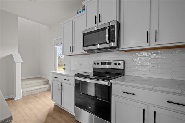 kitchen with appliances with stainless steel finishes, tasteful backsplash, light hardwood / wood-style floors, light stone counters, and white cabinetry