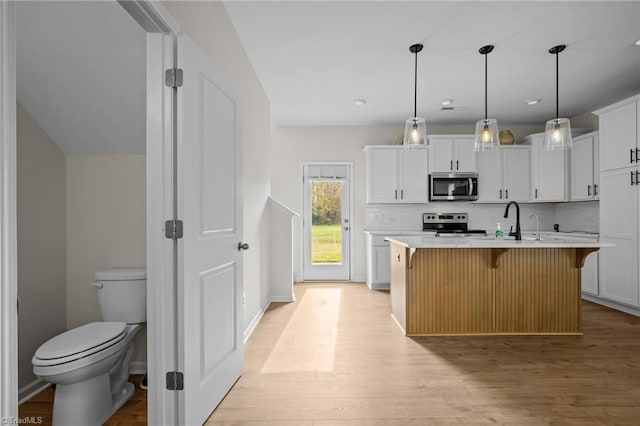 kitchen featuring stainless steel appliances, light hardwood / wood-style flooring, backsplash, a center island with sink, and white cabinets