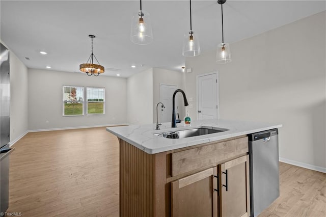 kitchen with light stone countertops, stainless steel dishwasher, decorative light fixtures, light hardwood / wood-style flooring, and an island with sink