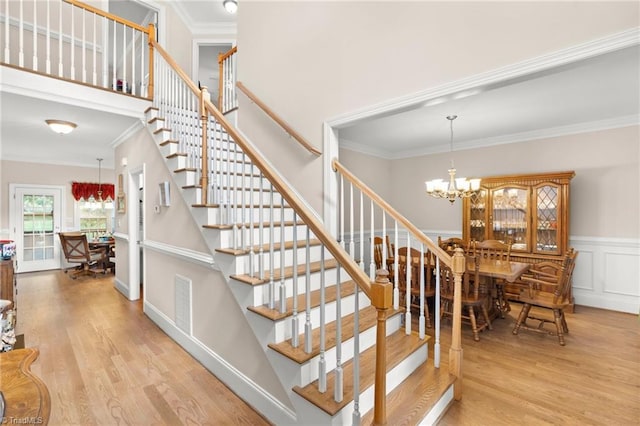 stairs with an inviting chandelier, hardwood / wood-style floors, and crown molding