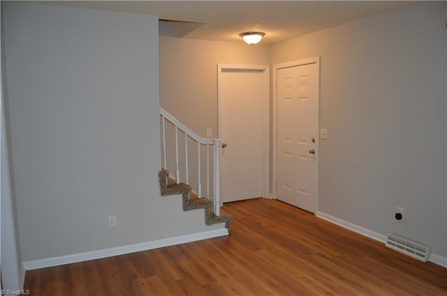 foyer featuring a textured ceiling, wood finished floors, visible vents, baseboards, and stairway