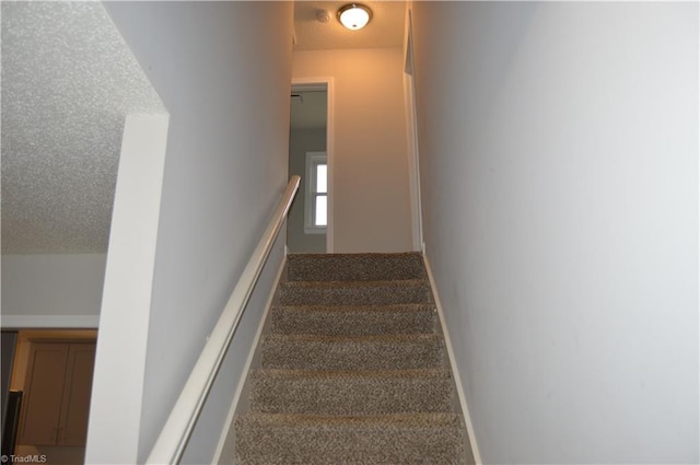 staircase with a textured ceiling, carpet flooring, and baseboards