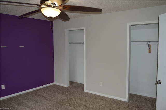 unfurnished bedroom with a textured ceiling, carpet floors, a ceiling fan, baseboards, and two closets